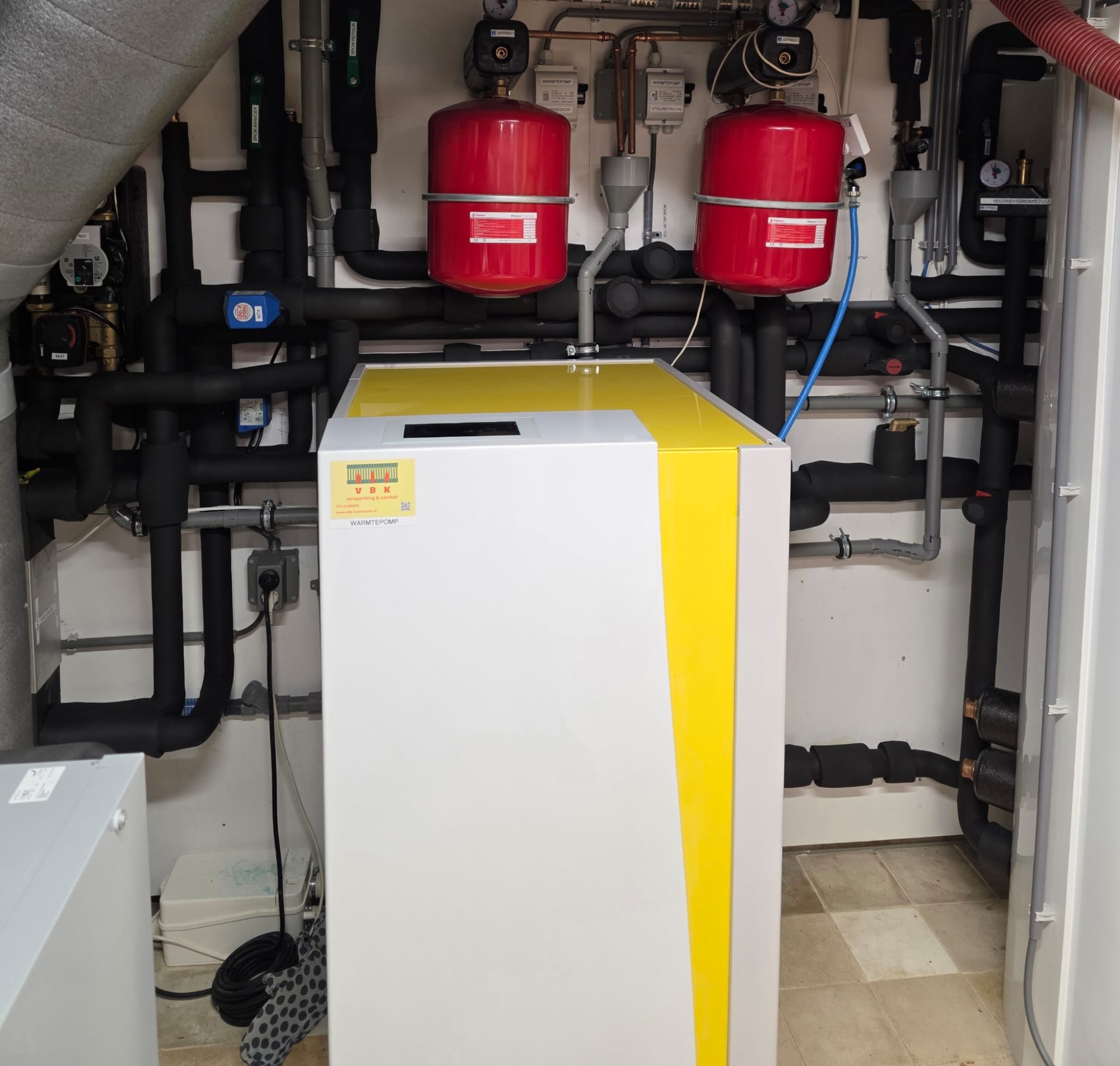 Warmtepomp binnen opstelling met buffervat en geïsoleerd leidingwerk